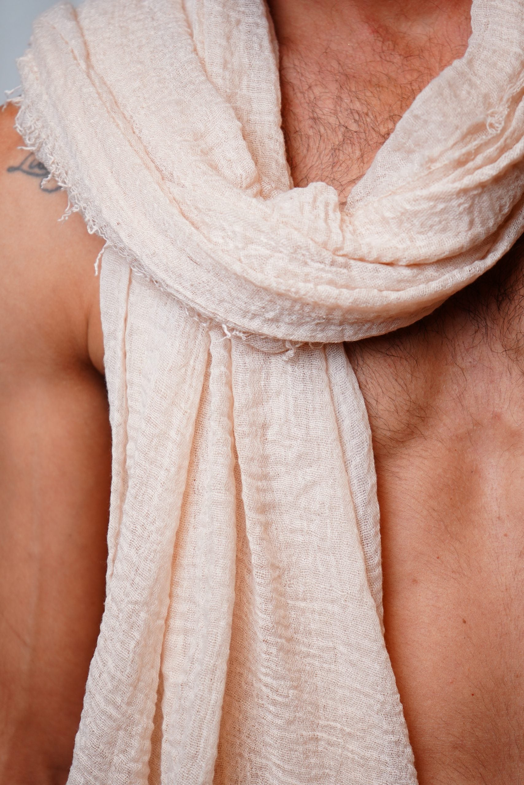 Close-up of person wearing a textured, light beige handmade scarf on bare chest