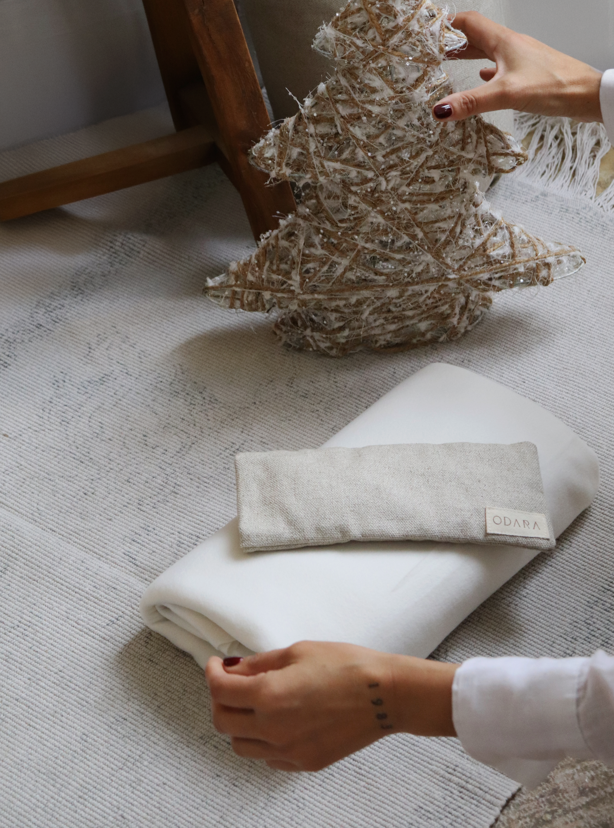 Hand placing rustic decorative tree beside folded white blanket and linen eye pillow