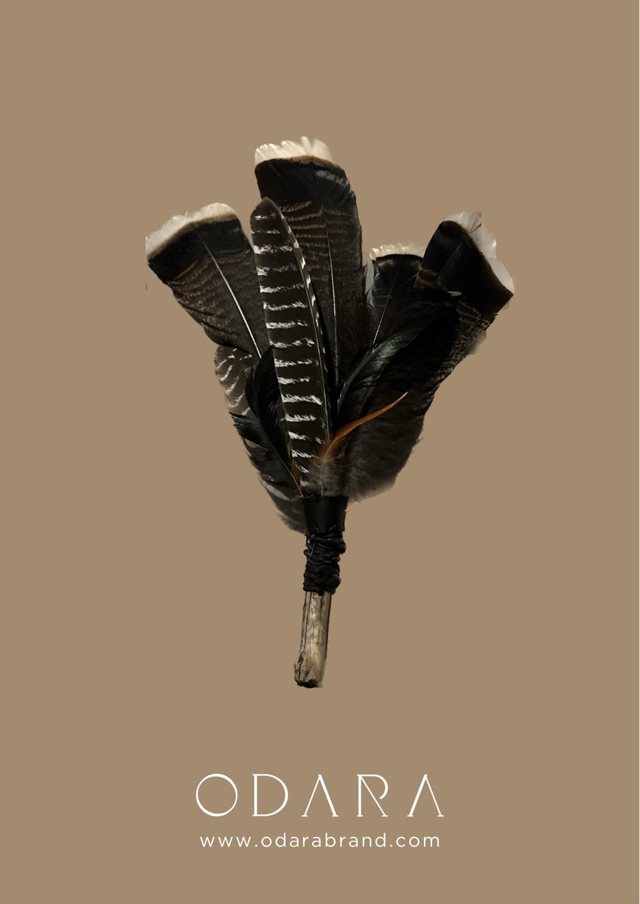 Handmade feather smudge fan with natural stick handle on beige background
