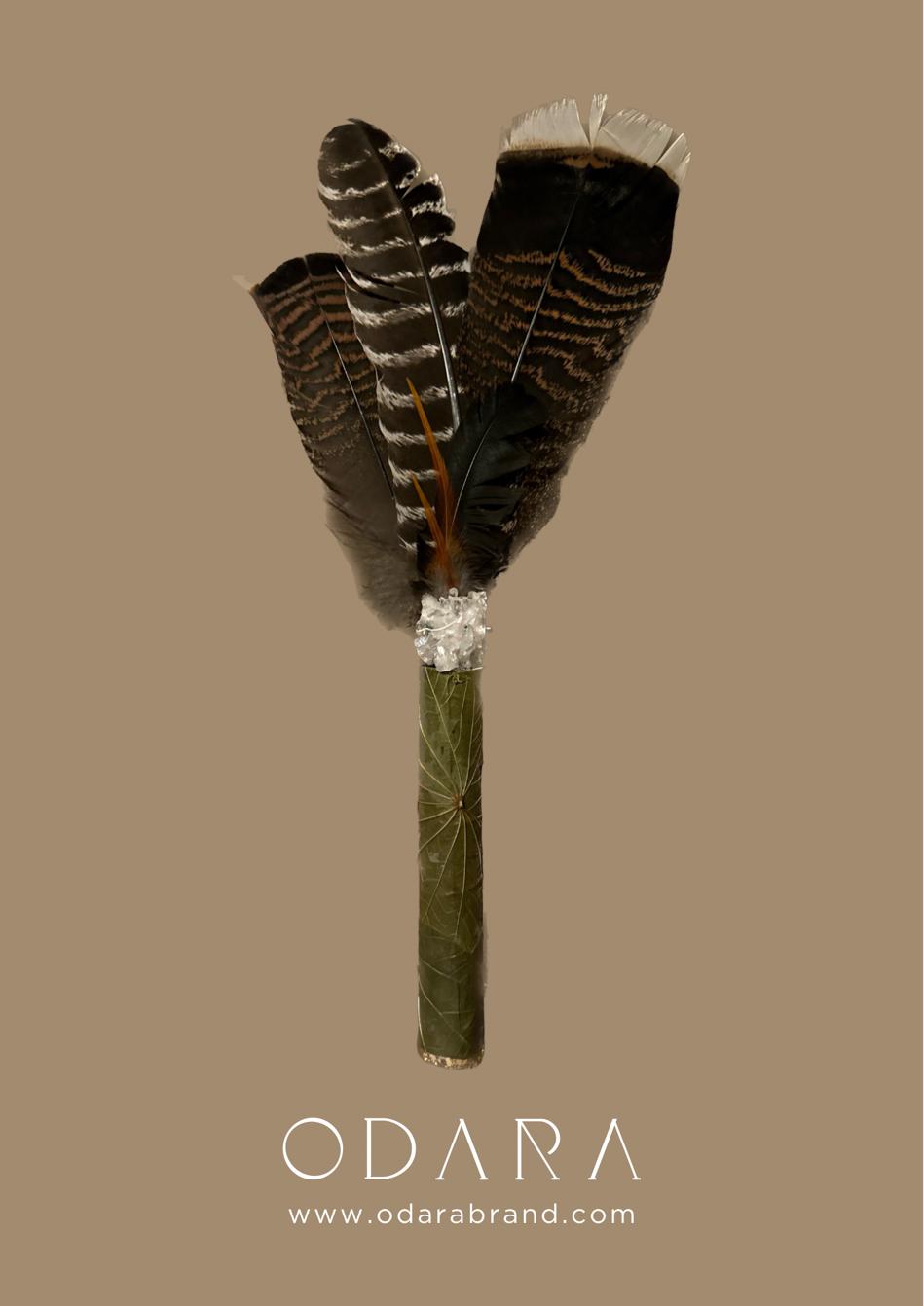Handmade fan with natural feathers and wrapped green leaf handle on neutral background
